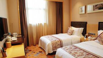 A hotel room with two beds, a desk with a chair, a television, and a window with curtains.