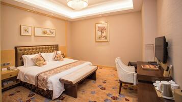 A hotel room with a large bed, bedside tables, a desk with a chair, a television, and artwork on the walls.