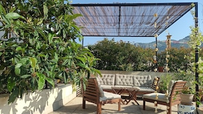 An outdoor seating area with a sofa, chairs, and a table, surrounded by potted plants and a decorative fence.