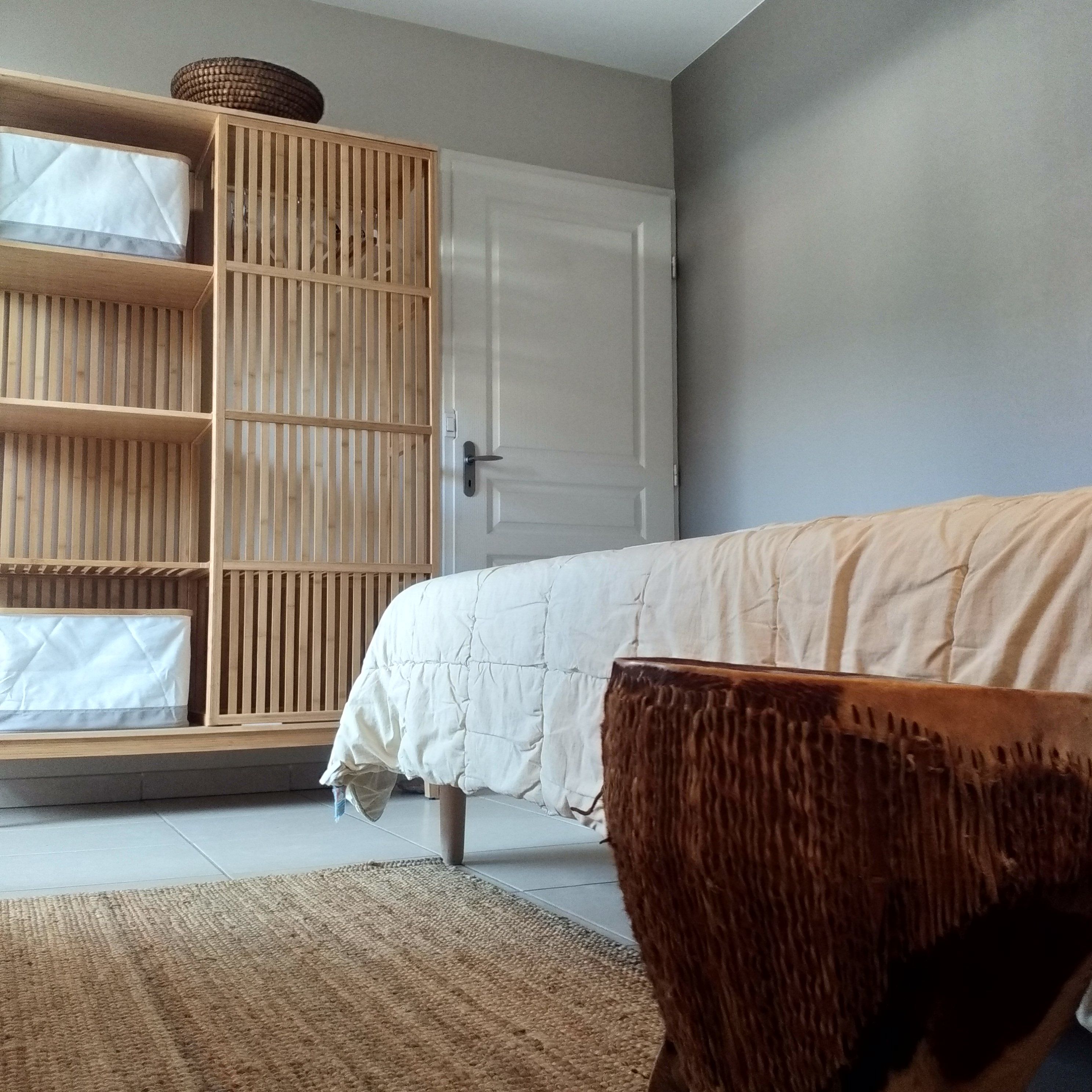 Un dormitorio con una cama, un armario de madera y una silla de fibras naturales.