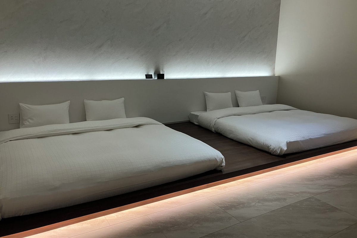 Habitación de hotel con dos camas, una plataforma de madera y un aplique de pared.