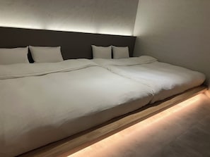 Una cama grande con cabecera y varias almohadas, suelo de madera y pared con textura.