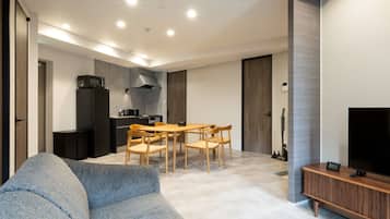 A modern living room with a sofa, dining table, chairs, a TV, and a kitchen area with appliances.