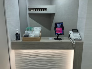 Un mostrador de recepción con una pantalla digital de bienvenida, un teléfono, y una presentación de gel hidroalcohólico y hisopos.