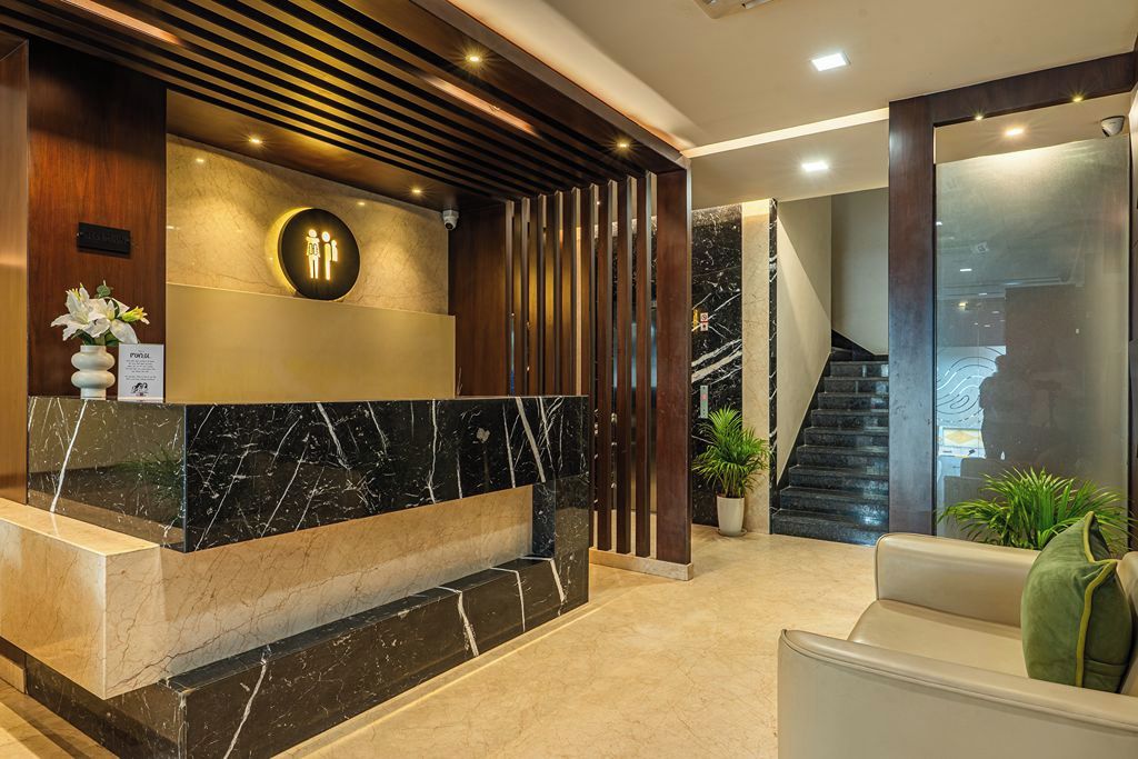 A reception area with a marble counter, a wooden panel wall, a round sign with figures, and a staircase in the background.