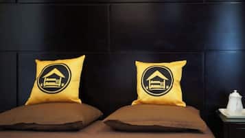 Una cama con dos almohadas, una mesita de noche con un objeto blanco y una pared oscura.
