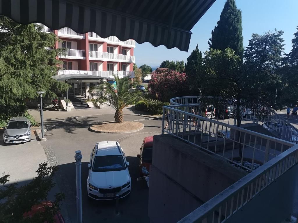 Ein Hotel mit roter Fassade, einer zentralen Palme und einem Parkplatz mit Autos.