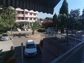 A hotel with a red facade, a palm tree in the center, and a parking area with cars. - Portofino Apartment (Izola)
