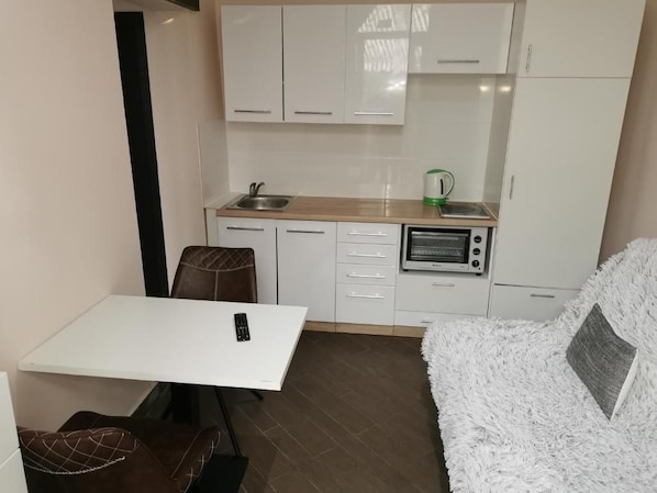 A compact kitchen with white cabinets, a microwave, and a kettle. There is a small table with a chair and a fluffy white sofa. - Portofino Apartment (Izola)