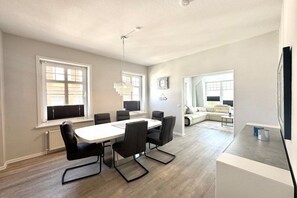 A modern living room with a dining area, large windows, and a flat-screen TV. - House with sea view - Apt. 1 (Wyk auf Föhr)