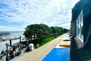 Eine Strandterrasse mit Sitzgelegenheiten im Freien, Blick auf das Meer und ein Weg zu einem Gebäude.