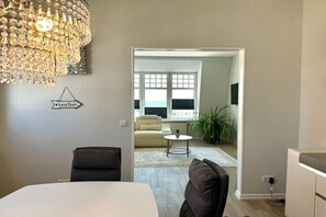 A hotel room with a bed, a chandelier, a sofa, a small table, and a view of the living area. - House with sea view - Apt. 1 (Wyk auf Föhr)