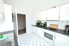 A kitchen with white cabinets, a microwave, a kettle, and a stove. - House with sea view - Apt. 1 (Wyk auf Föhr)