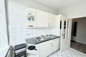 Eine Küche mit weißen Schränken, einer Arbeitsplatte, einem Spülbecken und einer Tür zu einem anderen Raum.