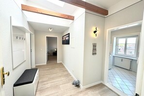 A hallway with a wooden ceiling beam, a white door, a small bench, and a window with a view of buildings. - House with sea view - Apt. 3 (Wyk auf Föhr)
