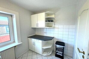 A small kitchen with white cabinets, a black countertop, and a trash bin labeled 'BEAUTIFUL pure'. - House with sea view - Apt. 3 (Wyk auf Föhr)