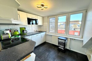 A modern kitchen with white cabinets, a black countertop, and a window with a view of buildings. - House with sea view - Apt. 4 (Wyk auf Föhr)