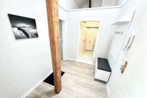 A narrow hallway with a wooden column, a black and white photograph on the wall, and a white door leading to a bathroom. - House with sea view - Apt. 4 (Wyk auf Föhr)