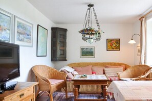 A cozy living room with wicker furniture, a flat-screen TV, and artwork on the walls. - Karoline House Apartment LISE (Hedehusum)