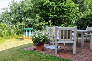 An outdoor patio with a brick floor, a wooden table and chairs, and a potted plant with white and purple flowers. - Karoline House Apartment LISE (Hedehusum)
