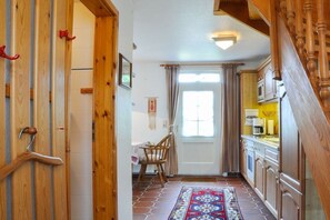 A narrow hallway with a wooden door, a chair, a patterned rug, and a kitchen area with cabinets and a microwave. - Karoline House Apartment LISE (Hedehusum)