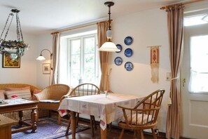 A dining area with a table set for four, surrounded by wicker chairs, a hanging light fixture, and a window with curtains. - Karoline House Apartment LISE (Hedehusum)