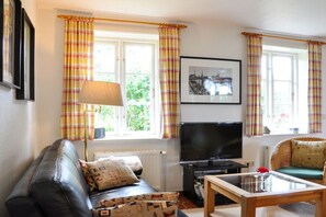 A living room with a sofa, a television, a coffee table, and a window with curtains. - Karoline House Apartment JULE (Hedehusum)