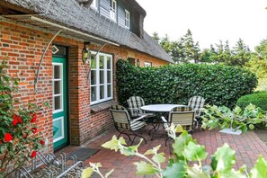 A brick house with a thatched roof, a green door, and a patio with a table and chairs. - Karoline House Apartment JULE (Hedehusum)