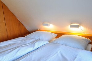 A bedroom with two beds, wooden headboard, and wall-mounted lighting. - Karoline House Apartment JULE (Hedehusum)