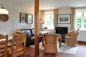 A living room with a black leather sofa, wicker chairs, a television, and framed pictures on the wall. - Karoline House Apartment JULE (Hedehusum)