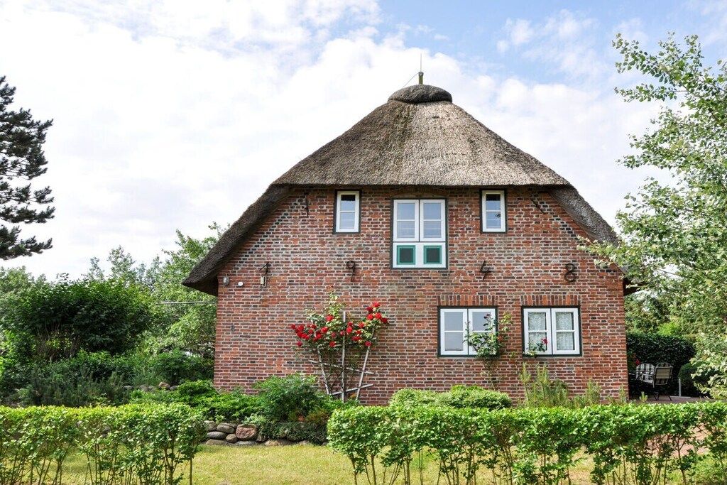 Une maison en briques avec un toit de chaume, entourée de verdure et d’un jardin bien entretenu.