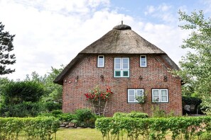 A brick house with a thatched roof, surrounded by greenery and a well-maintained garden. - Karoline House Apartment JULE (Hedehusum)