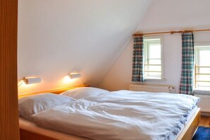 A bedroom with a bed, two bedside lamps, a window with curtains, and a radiator. - Karoline House Apartment JULE (Hedehusum)