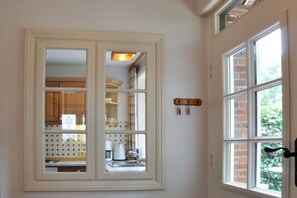 A room with a white-framed window, a kitchen visible through the window, and a door with a black handle. - Karoline House Apartment JULE (Hedehusum)