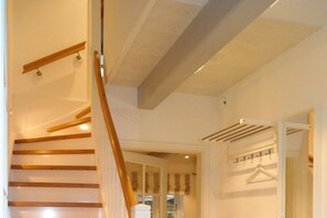 Eine Treppe mit Holzdielen und einer Handläufe, die zu einem Raum mit einer weißen Wand und einem an der Wand befestigten Kleiderhaken führt.