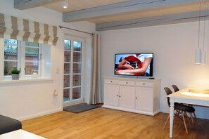 Ein modernes Wohnzimmer mit Fernseher, Essbereich und großem Fenster mit Vorhängen.
