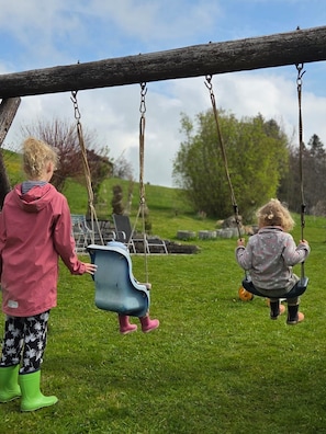 Zwei Kinder schaukeln auf einer Schaukel im grünen Freigelände.