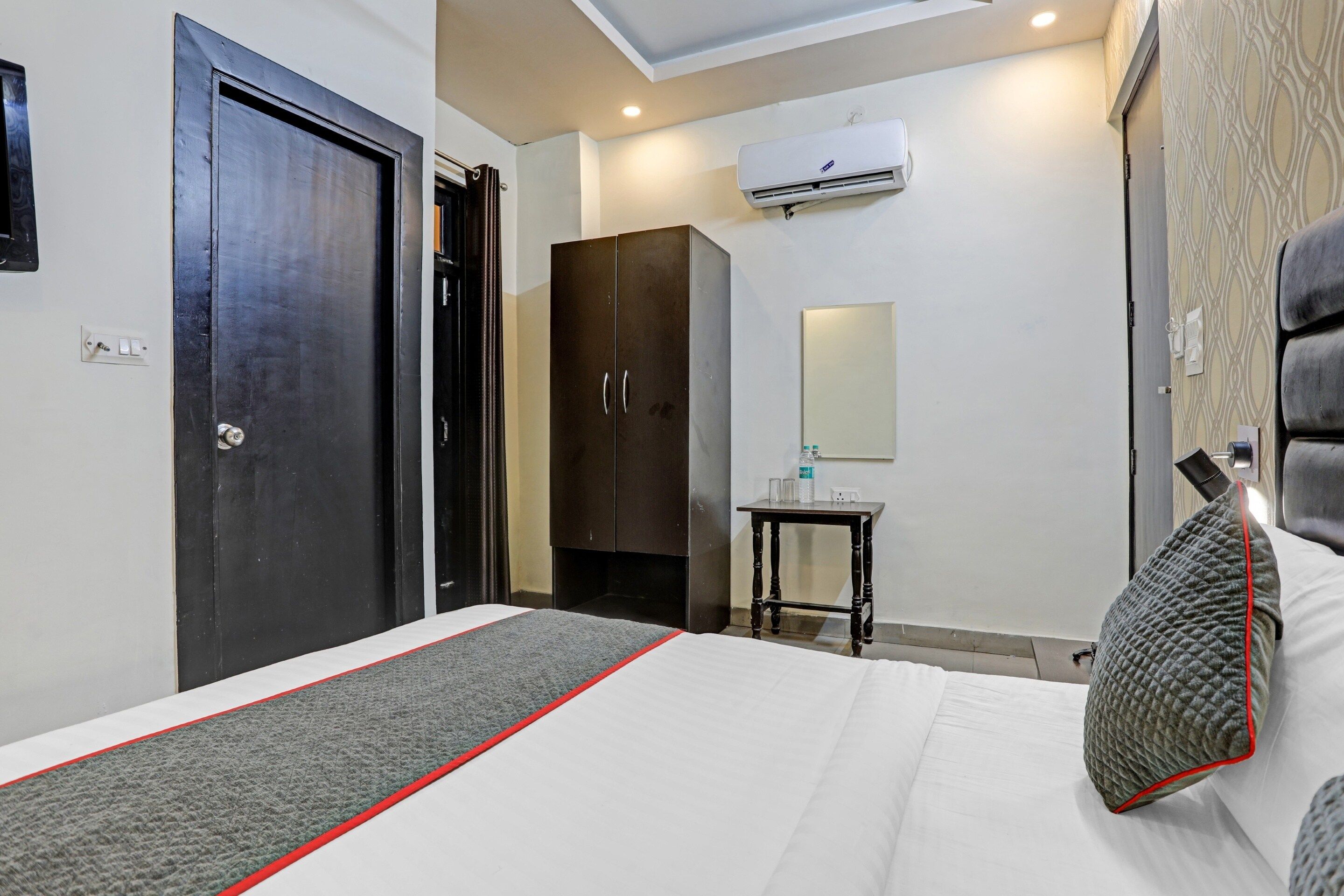 Habitación de hotel con cama, armario, una mesita de noche con espejo y equipo de aire acondicionado en la pared.