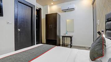 Habitación de hotel con cama, armario, una mesita de noche con espejo y equipo de aire acondicionado en la pared.