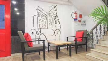 Un hall con puerta roja, dos sillones con cojines rojos, una mesa de madera y un gran mural blanco y negro en la pared.