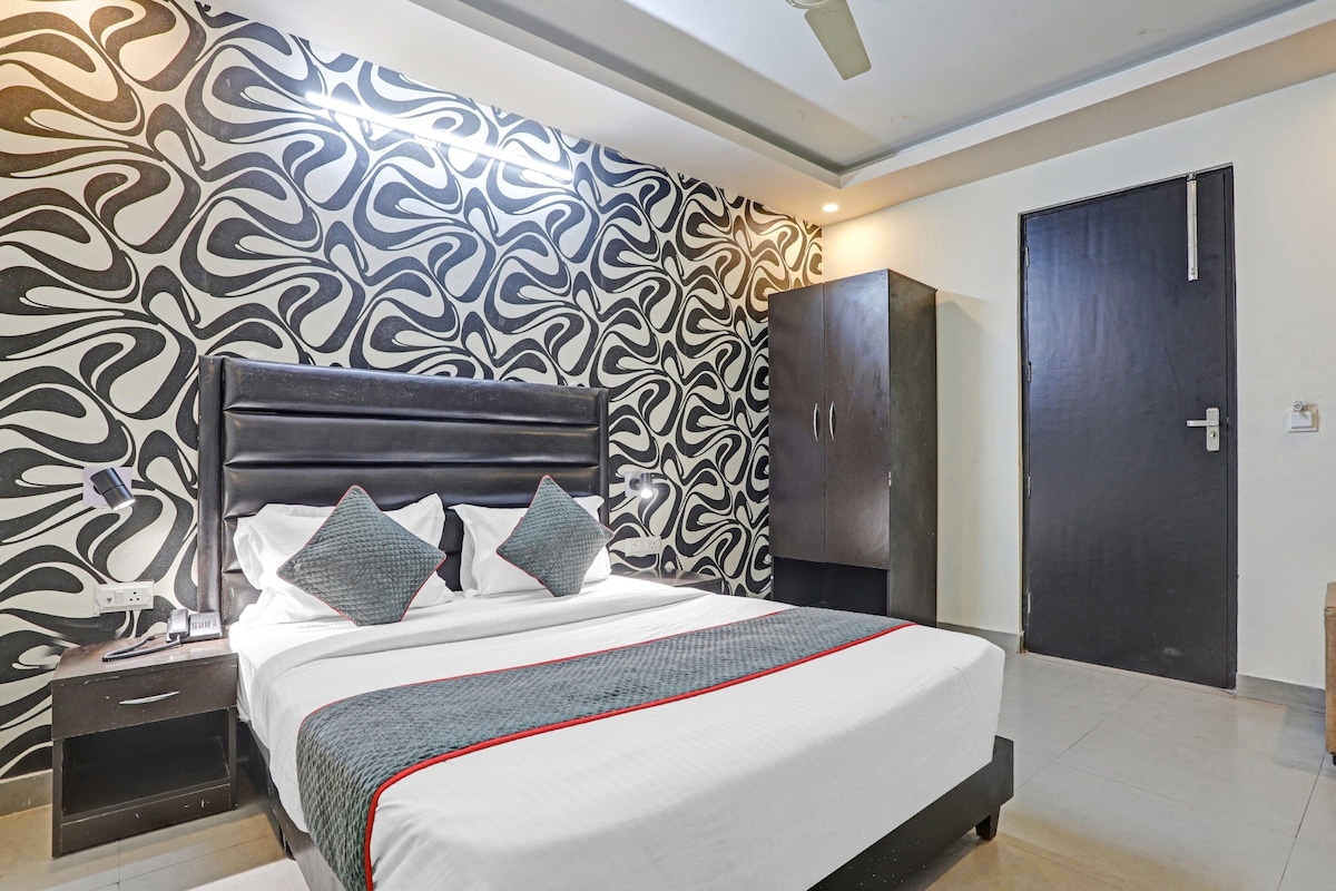 A modern bedroom with a patterned wallpaper, a bed with pillows, a bedside table with a phone, and a wardrobe.