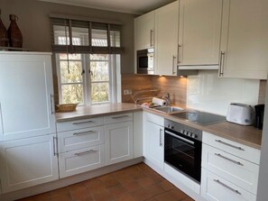 A kitchen with white cabinets, a built-in oven, a microwave, and a window with blinds. - 8a in the Building on Neuer Weg (Wrixum)