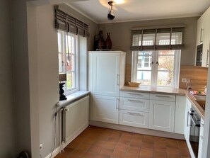 A kitchen with white cabinets, a radiator, a window with blinds, and a ceiling light fixture. - 8a in the Building on Neuer Weg (Wrixum)