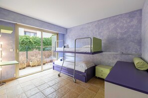 Quarto com beliche, uma pequena escrivaninha, cadeira e porta de vidro que se abre para área externa.