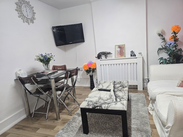A modern living room with a flat-screen TV mounted on the wall, a dining table with chairs, a sofa, and a coffee table. - Charming 2-bed House in Greater London With Central Access (Croydon)