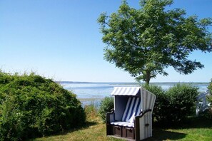 A beach chair with a striped canopy, positioned on grass near a tree and a body of water. - Helene's little house (Gelting)