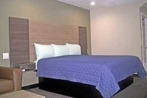 A hotel room with a bed, a nightstand, a chair, and a door. - Scot Tish Inns And Suites (Beaumont)