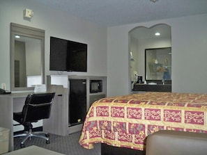 A hotel room with a bed, a desk, a chair, a television, and a mirror. - Scot Tish Inns And Suites (Beaumont)