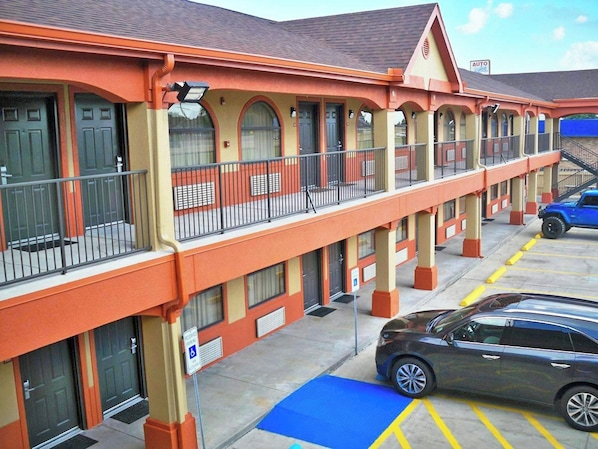 A motel with a row of rooms, a parking area, and a blue car parked in front. - Scot Tish Inns And Suites (Beaumont)