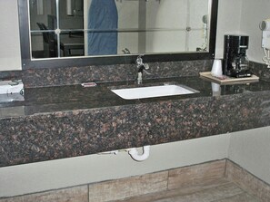 A bathroom with a granite countertop, a sink, a mirror, and a coffee maker. - Scot Tish Inns And Suites (Beaumont)